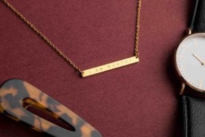 Product photography Gold I Am Worthy Necklace By Jenna Kutcher on red paper with accessories