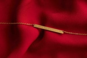 gold I Am Worthy necklace by Jenna Kutcher on red silk like fabric product photography